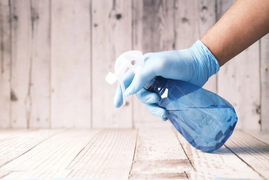 Close-up view of a hand cleaning a window outdoors with a squeegee, wearing yellow gloves.